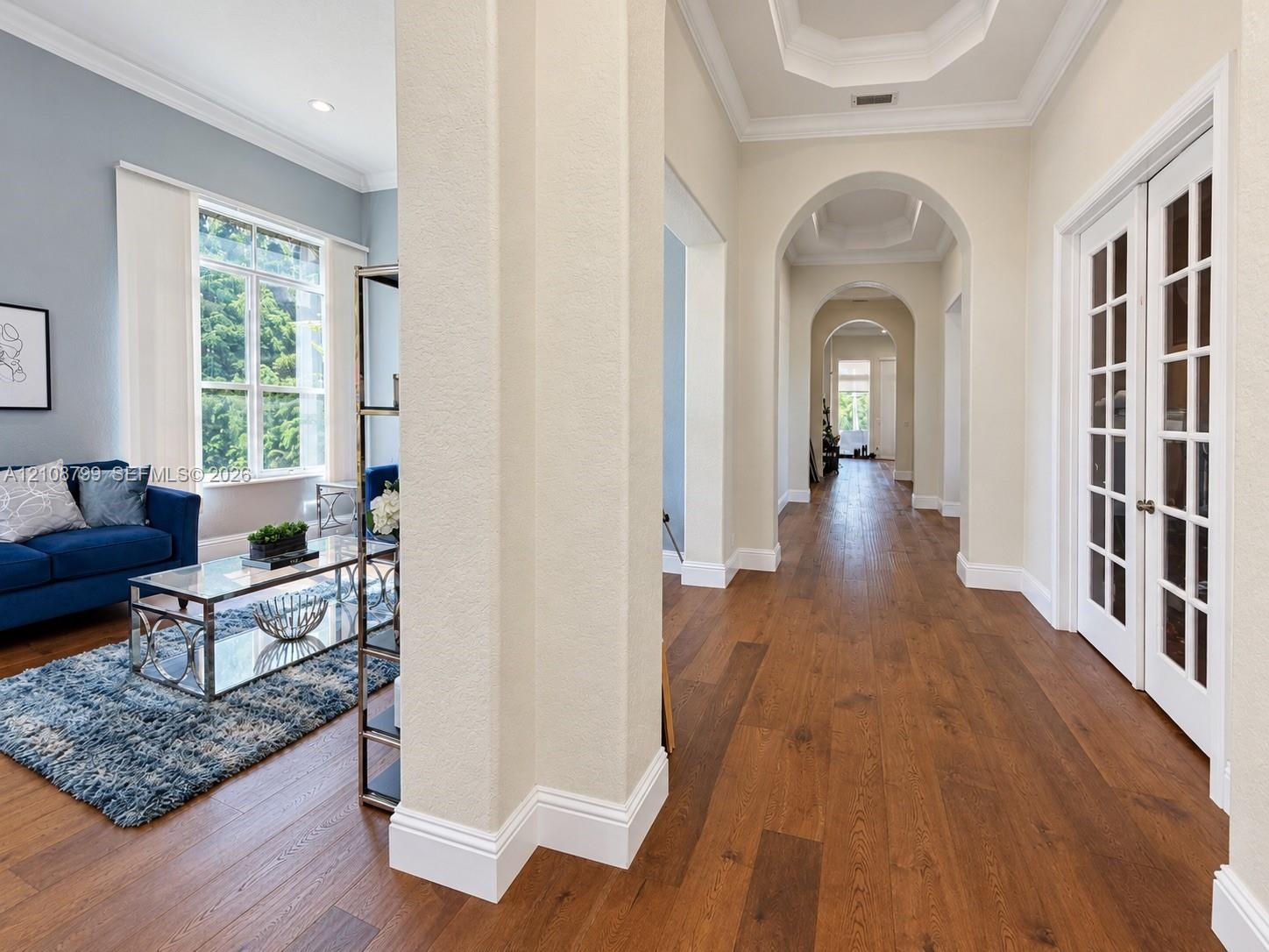 Foyer featuring wood-finish flooring, recessed tray ceilings, arched entryways, and white-trimmed glass-paneled French doors