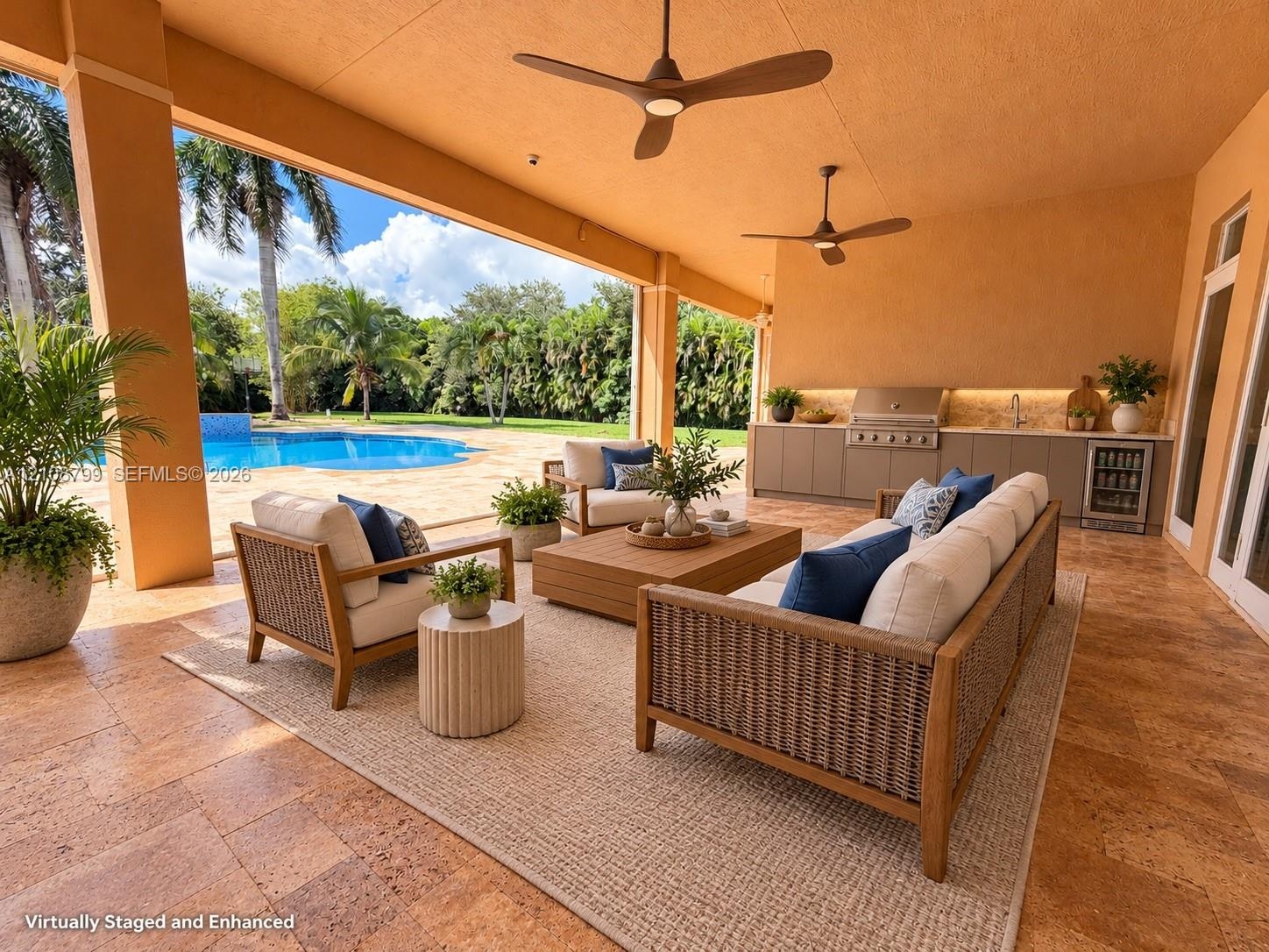 Covered outdoor living space featuring stone flooring, dual ceiling fans, built-in outdoor kitchen with stainless steel grill, and an in-ground swimmi