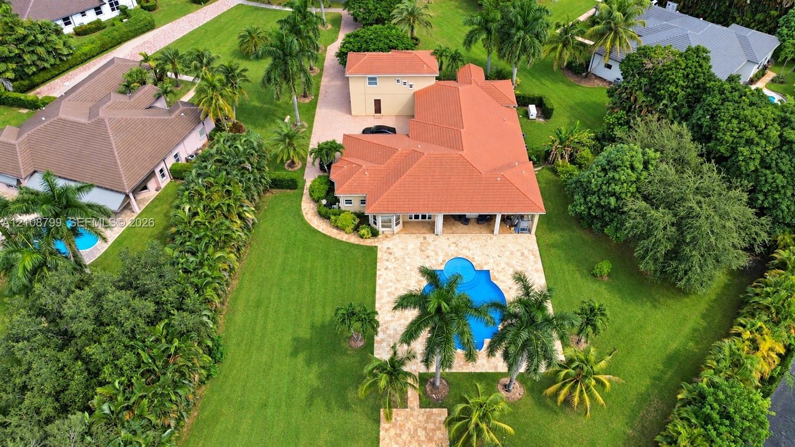 Expansive property featuring a multi-level structure with a terracotta tile roof, a stone-paved patio, a custom-shaped swimming pool, and mature palm 