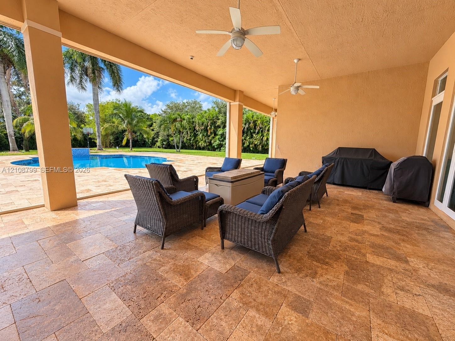Covered patio featuring stone-tiled flooring, dual ceiling fans, recessed lighting, and a pool deck