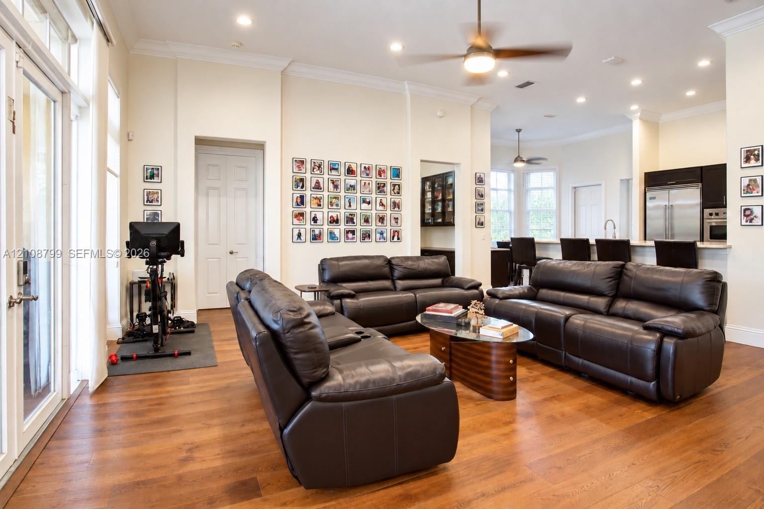 Open-concept interior featuring wood-finish flooring, recessed lighting, crown molding, double glass doors, and a breakfast bar