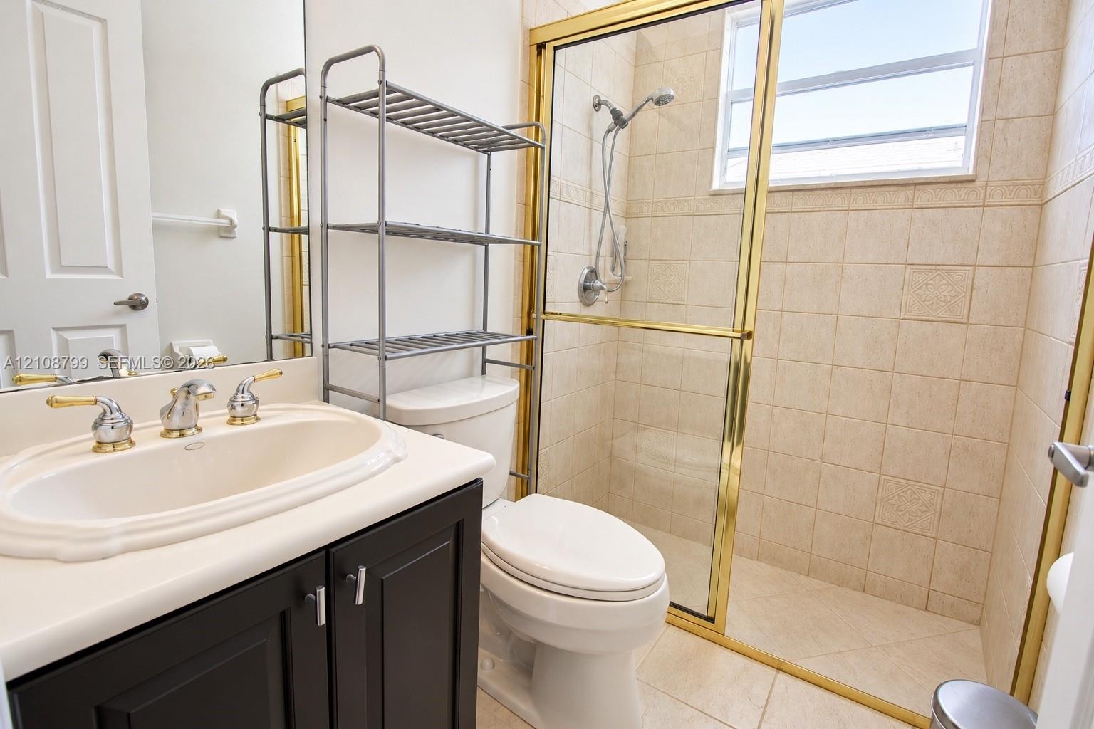 Bathroom featuring a dark wood-finish vanity, integrated oval sink, brass-tone hardware, shower enclosure with glass sliding doors, and tiled wall fin