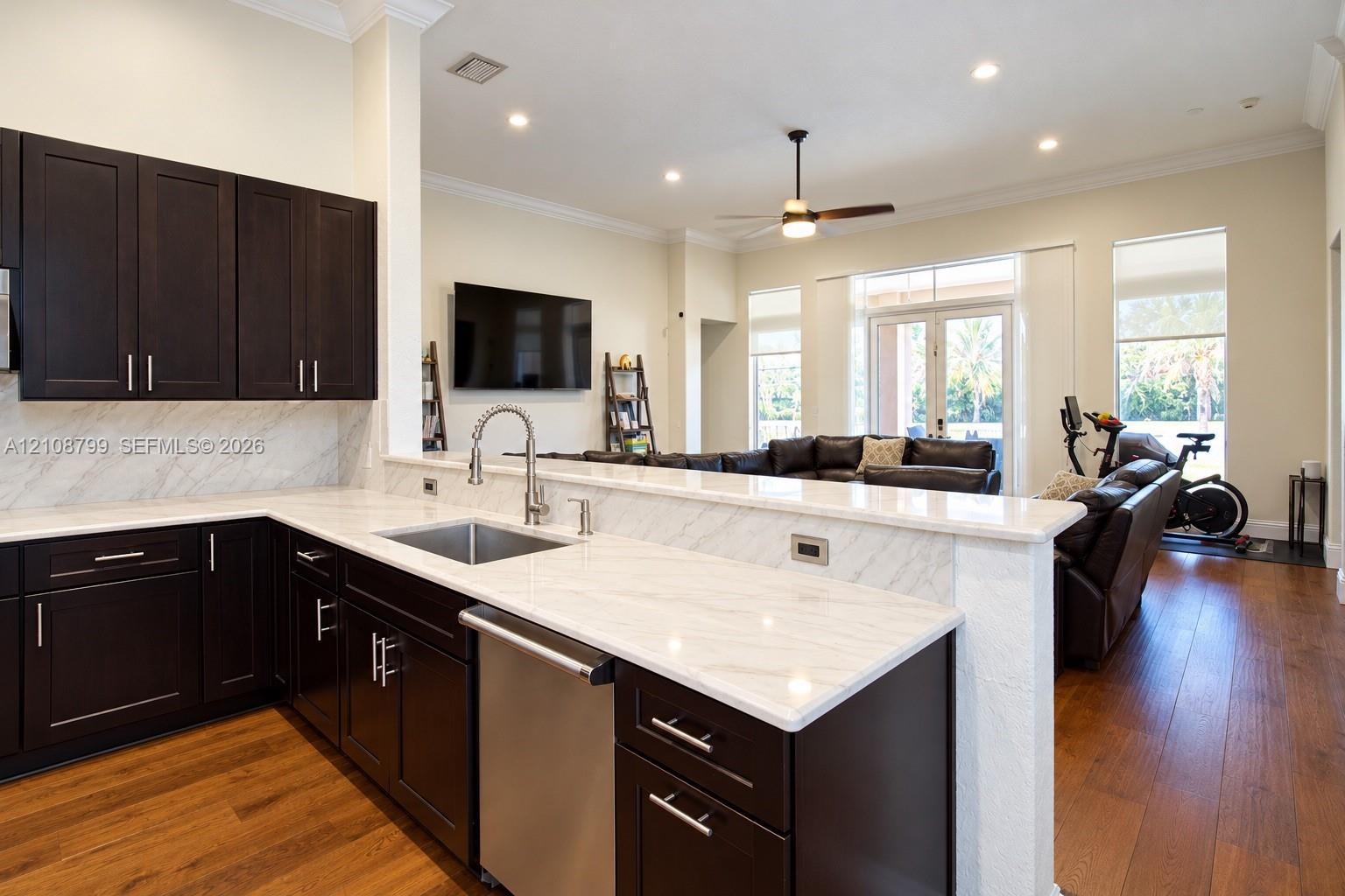 Kitchen featuring dark-finish cabinetry, stone-surface countertops, stone-surface backsplash, stainless steel undermount sink, and wood-finish floorin