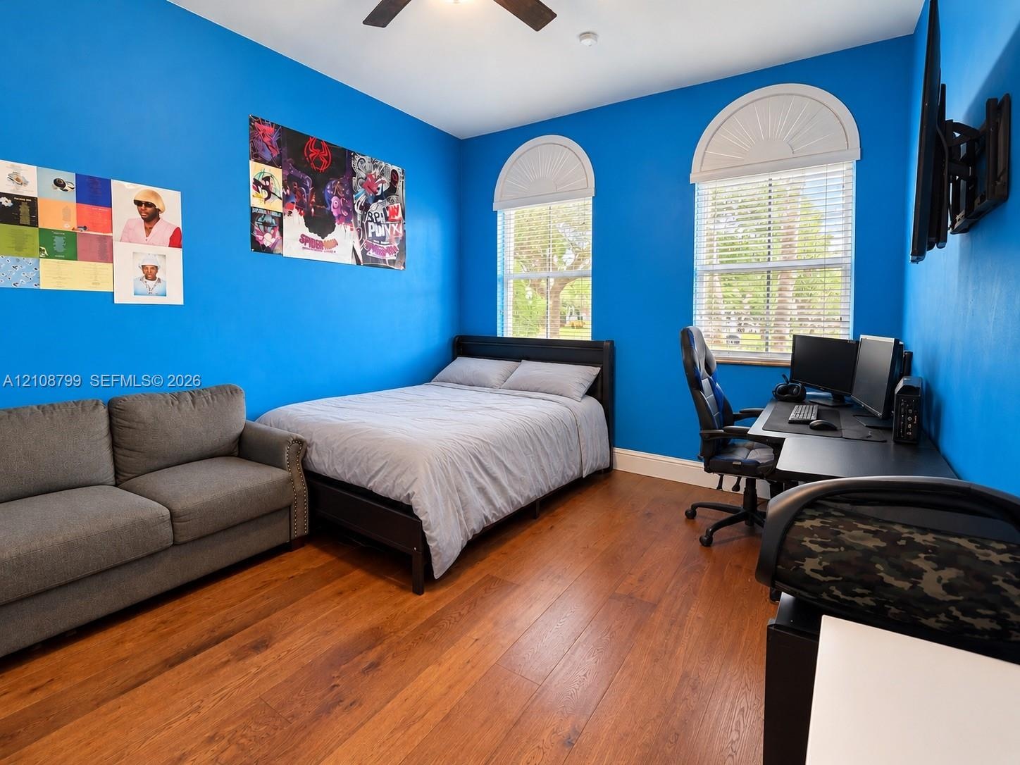 Room featuring wood-finish flooring, two arched windows with decorative transoms, and a ceiling fan