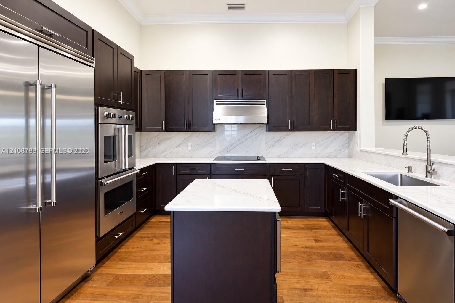 Kitchen featuring dark wood cabinetry, a central island with a stone countertop, stone slab backsplash, stainless steel appliances, and wood-finish fl