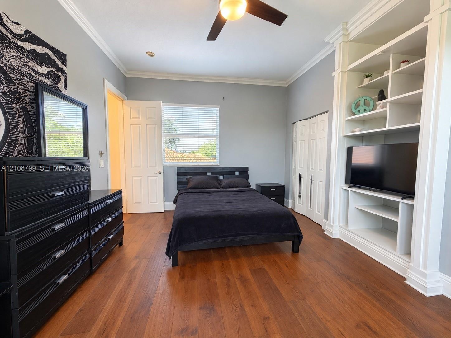 Room featuring custom built-in floor-to-ceiling shelving, wood-finish flooring, crown molding, and a ceiling fan with integrated lighting