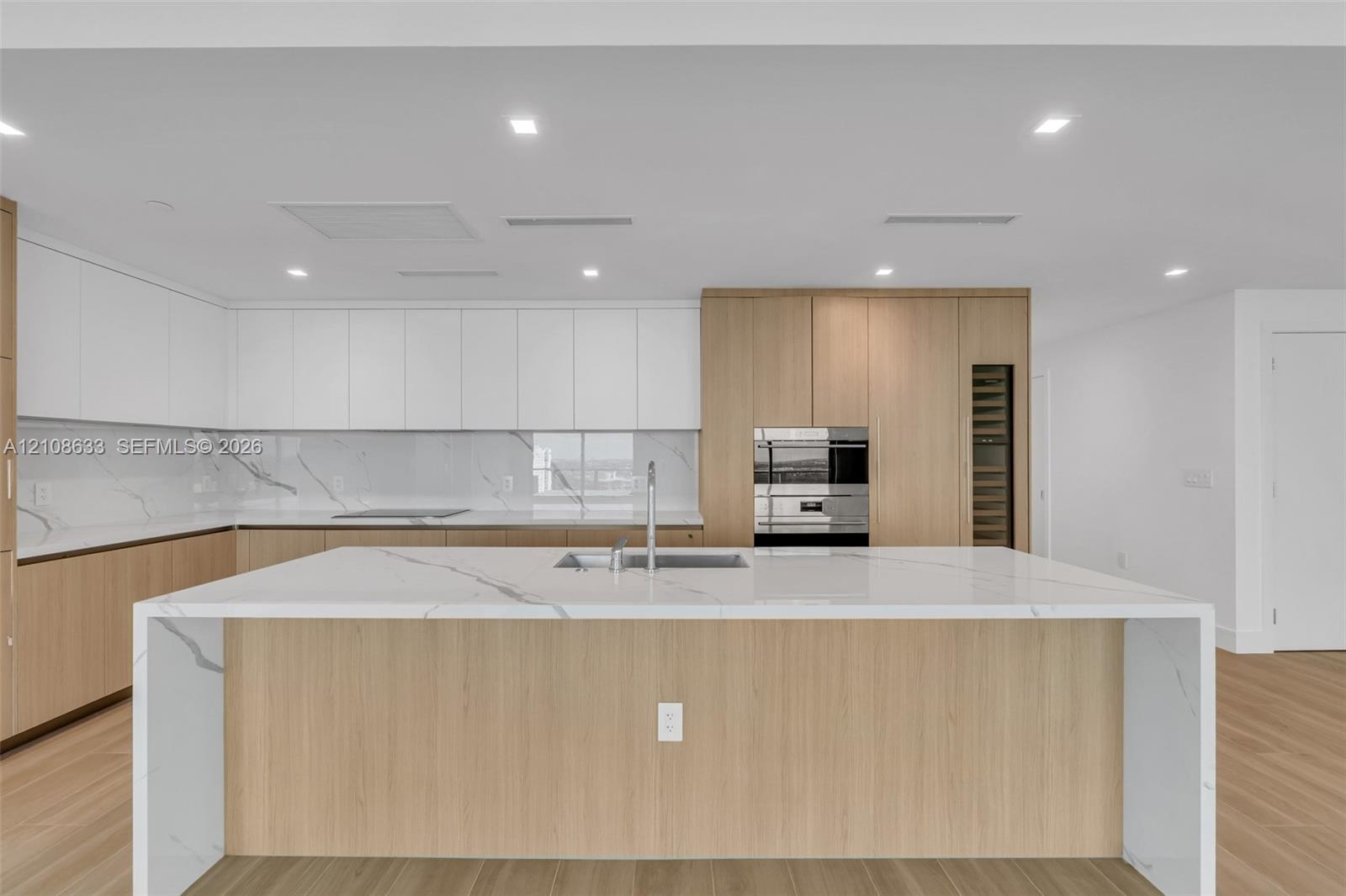 Modern kitchen featuring a waterfall-edge island with stone-finish countertops, two-tone cabinetry, recessed ceiling lighting, a built-in oven, and wo