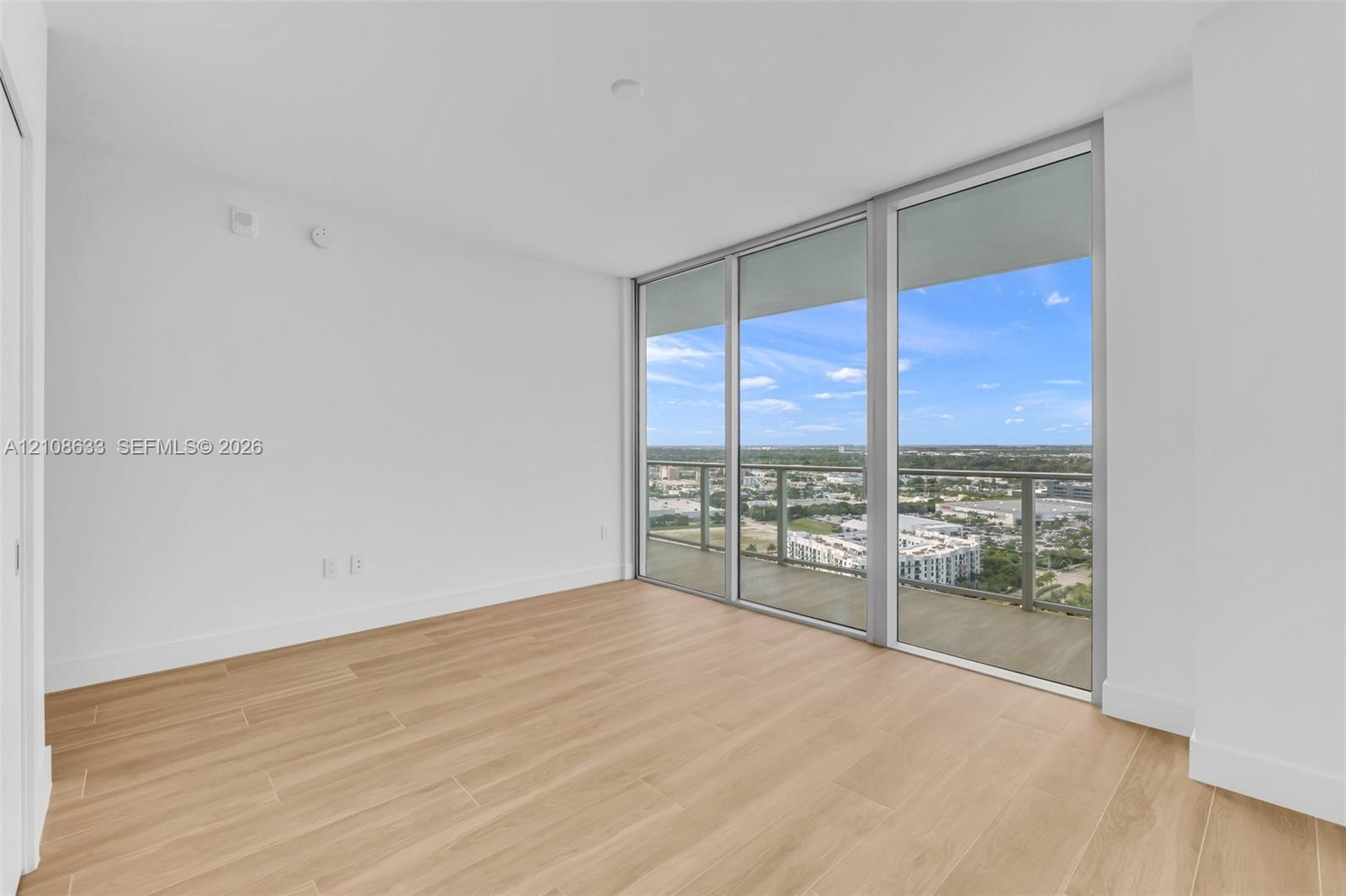 Floor-to-ceiling windows, wood-finish flooring, and access to a private balcony with a metal railing
