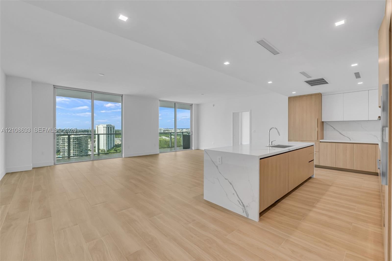 Open-concept interior featuring light wood-finish flooring, a kitchen island with stone-finish waterfall countertop, integrated cabinetry, and floor-t