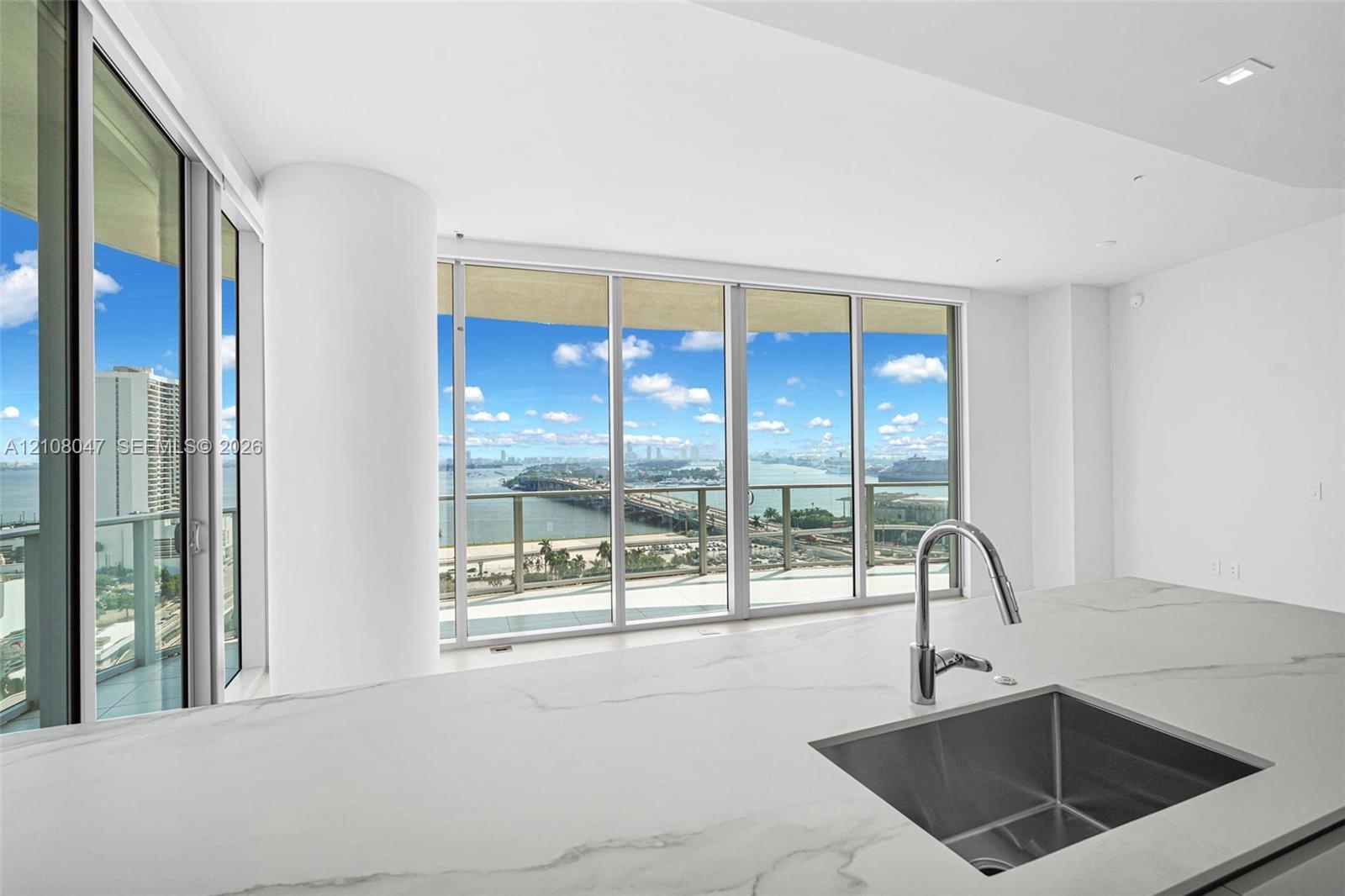 Expansive floor-to-ceiling windows, white countertop with veining, under-mount stainless steel sink, contemporary chrome pull-down faucet, recessed ce