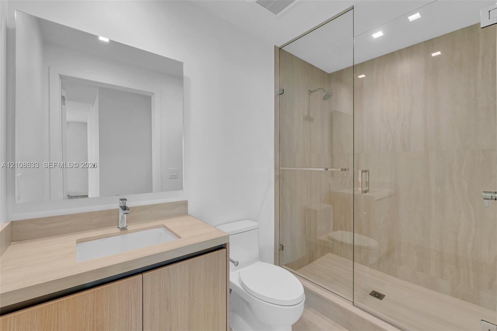 Bathroom featuring a wood-finish vanity with an integrated sink, large frameless wall mirror, walk-in shower with floor-to-ceiling tile, glass enclosu