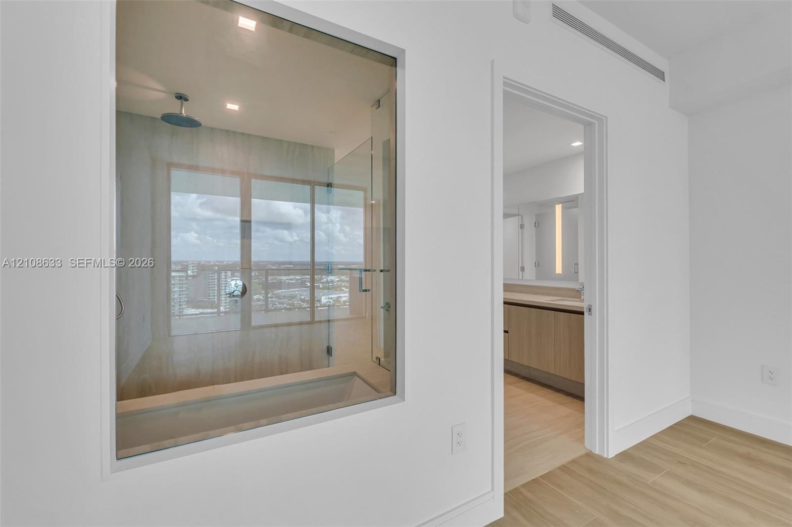 Interior space featuring wood-finish flooring, a glass-enclosed soaking tub with a ceiling-mounted rainfall showerhead, and dual-vanity cabinetry with