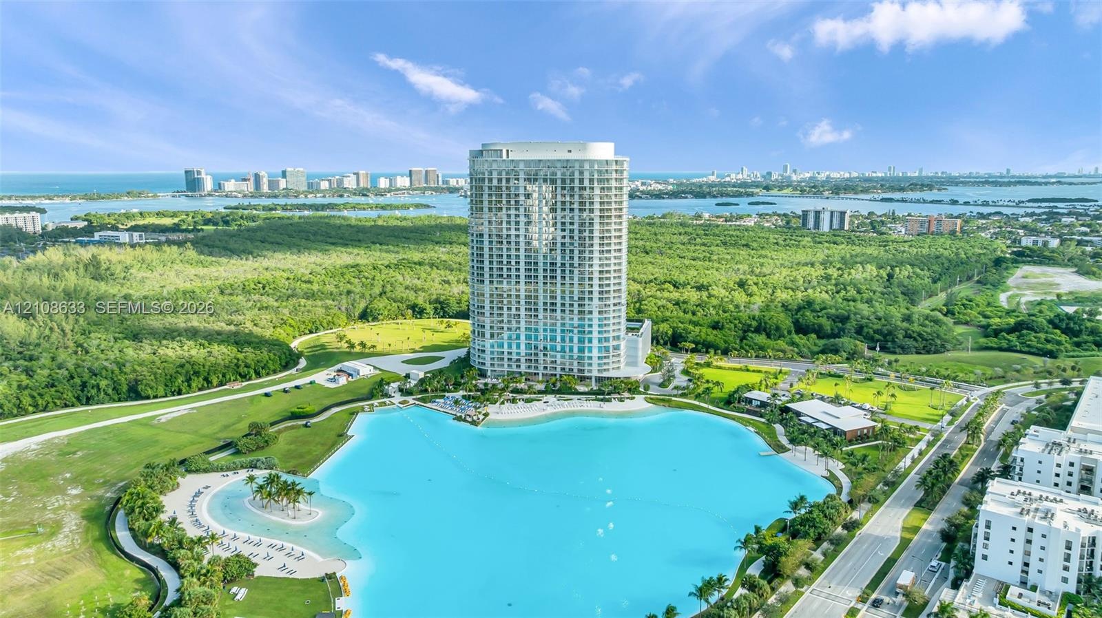 High-rise residential tower featuring a glass-facade exterior, expansive recreational lagoon with sandy shoreline, and manicured surrounding grounds