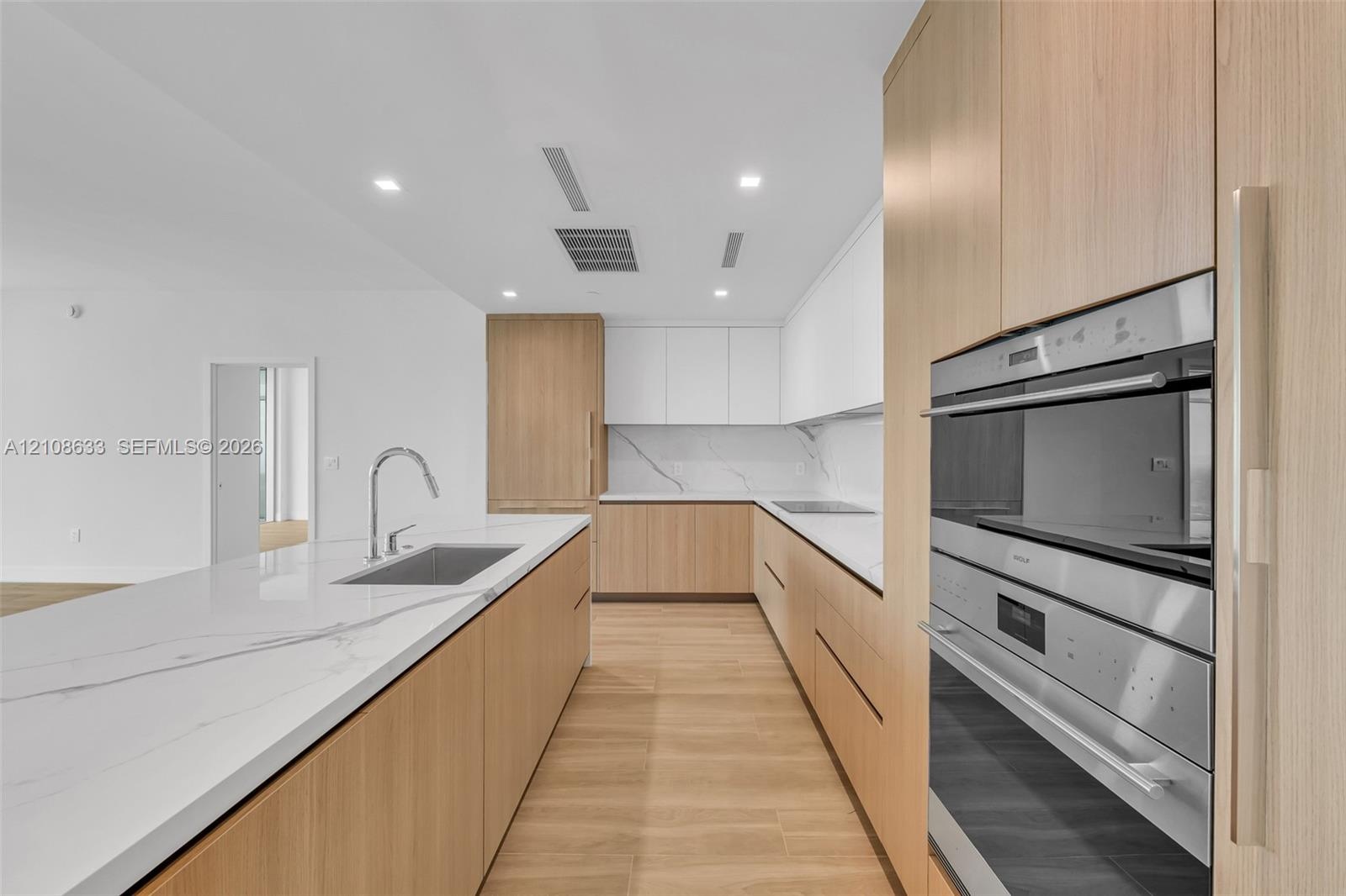 Kitchen featuring wood-finish cabinetry, white stone-look countertops with veining, a stainless steel undermount sink with a gooseneck faucet, and int