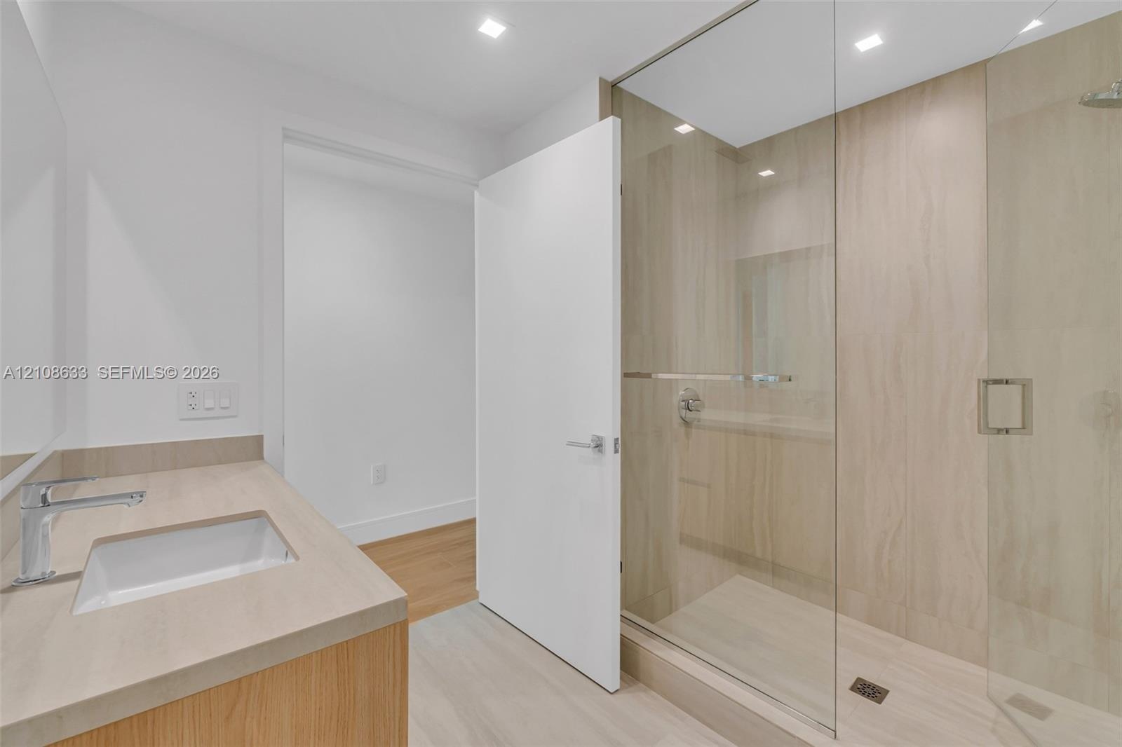 Modern bathroom featuring a wood-finish vanity with a solid-surface countertop, an integrated rectangular sink, a glass-enclosed walk-in shower with f
