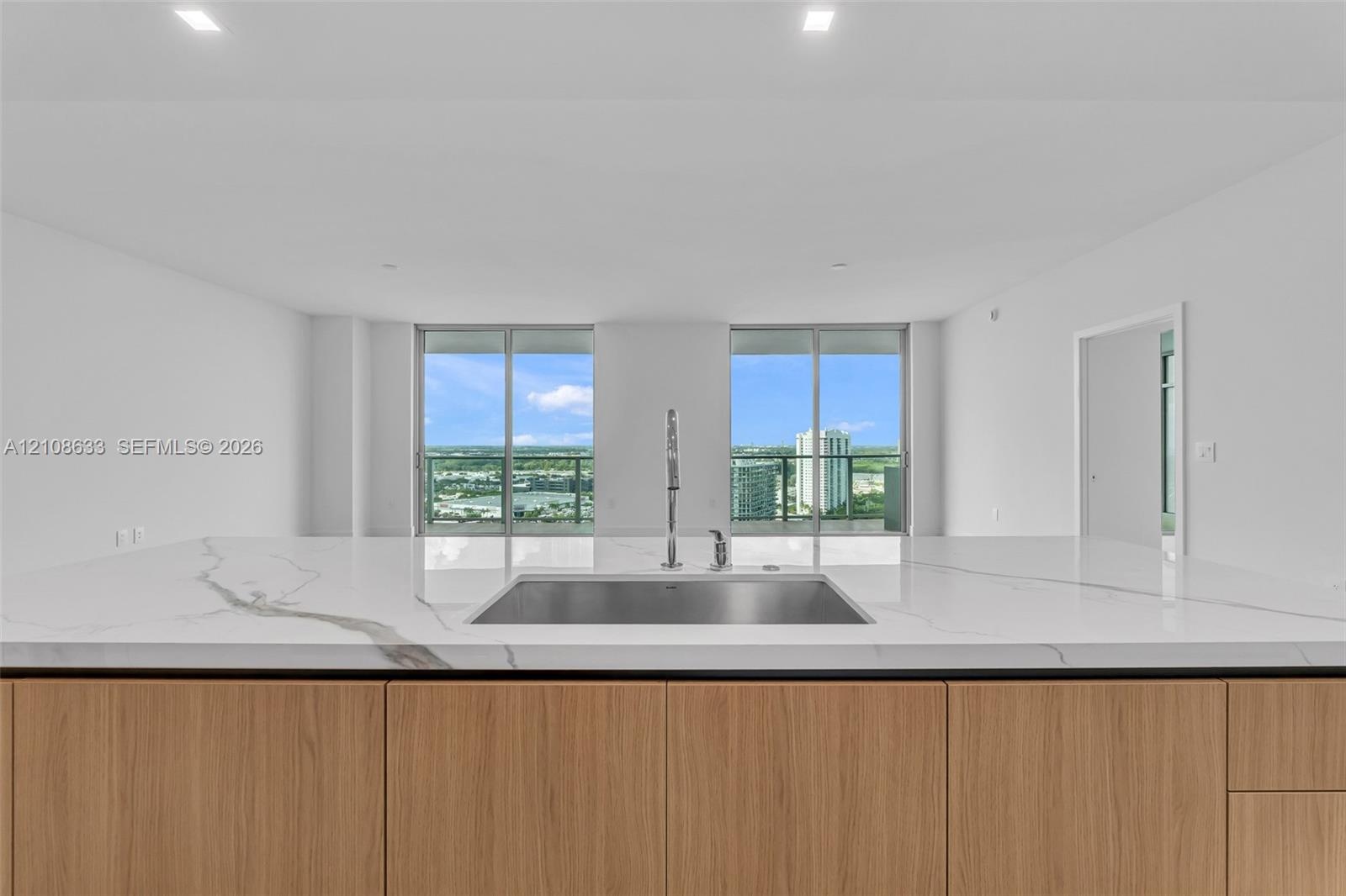 Kitchen island with waterfall-edge stone countertop, undermount stainless steel rectangular sink, tall arching faucet, wood-finish cabinetry, and floo