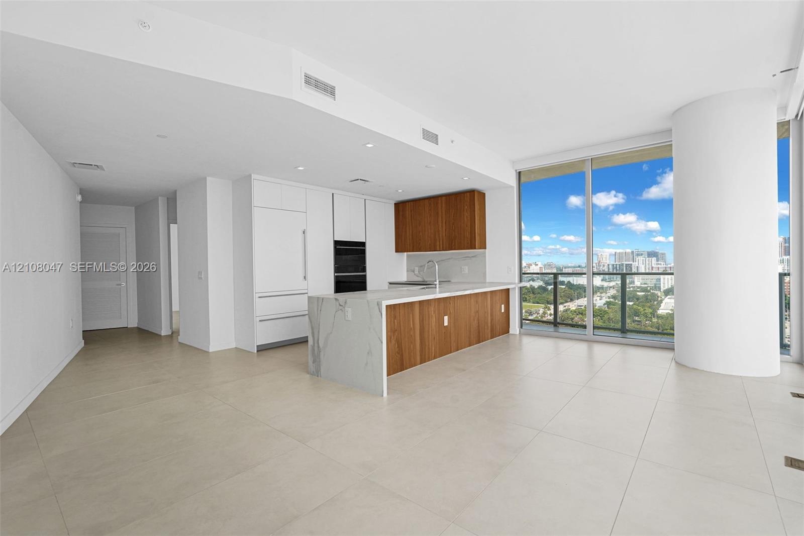 Open concept living area with light-toned tile flooring, floor-to-ceiling windows, and a modern kitchen featuring wood-finish cabinetry, integrated ap