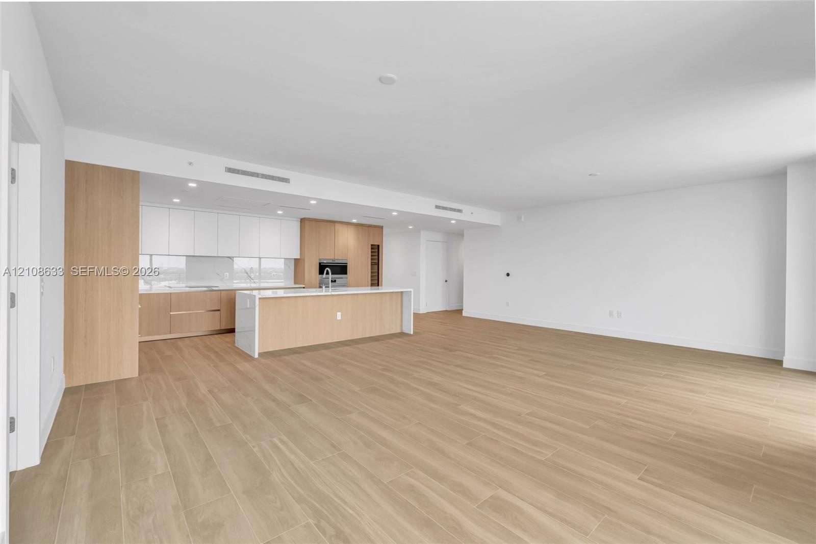 Open-concept interior featuring wood-finish flooring, recessed lighting, and a kitchen equipped with flat-panel wood cabinetry, white stone-surface co