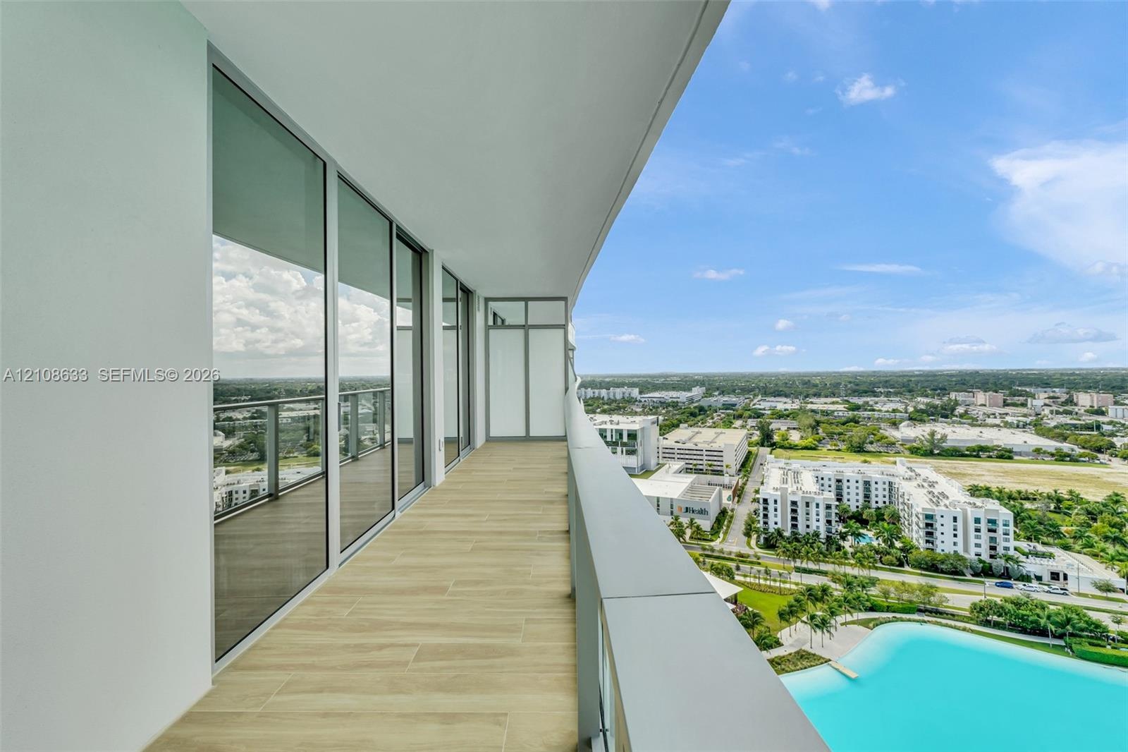 Covered balcony featuring expansive glass panel railings, wood-finish tile flooring, and floor-to-ceiling glass wall panels