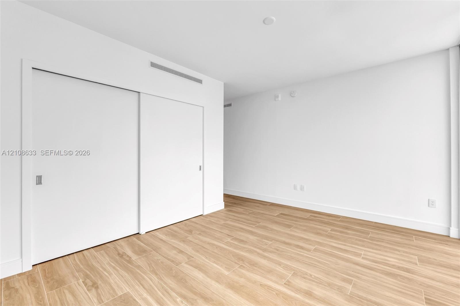 Interior space featuring wood-finish flooring, crisp white walls, and a large closet with sliding doors