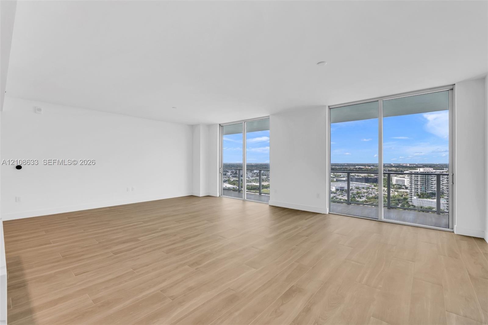 Open-concept living space featuring wood-finish flooring, floor-to-ceiling glass sliding doors, and exterior balcony access