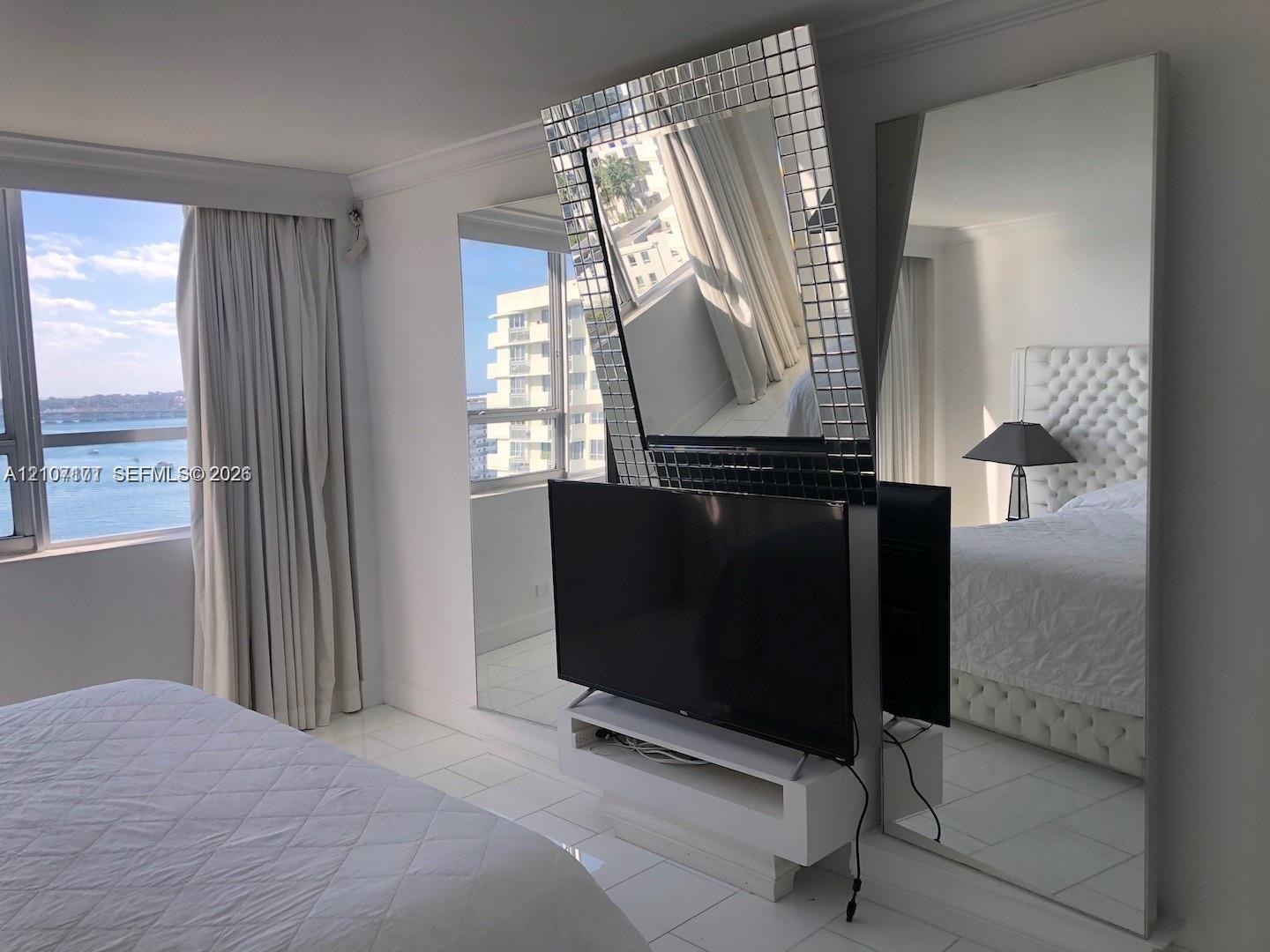 Floor-to-ceiling windows, white tile flooring, built-in white media console, and floor-to-ceiling mirrored wall panels