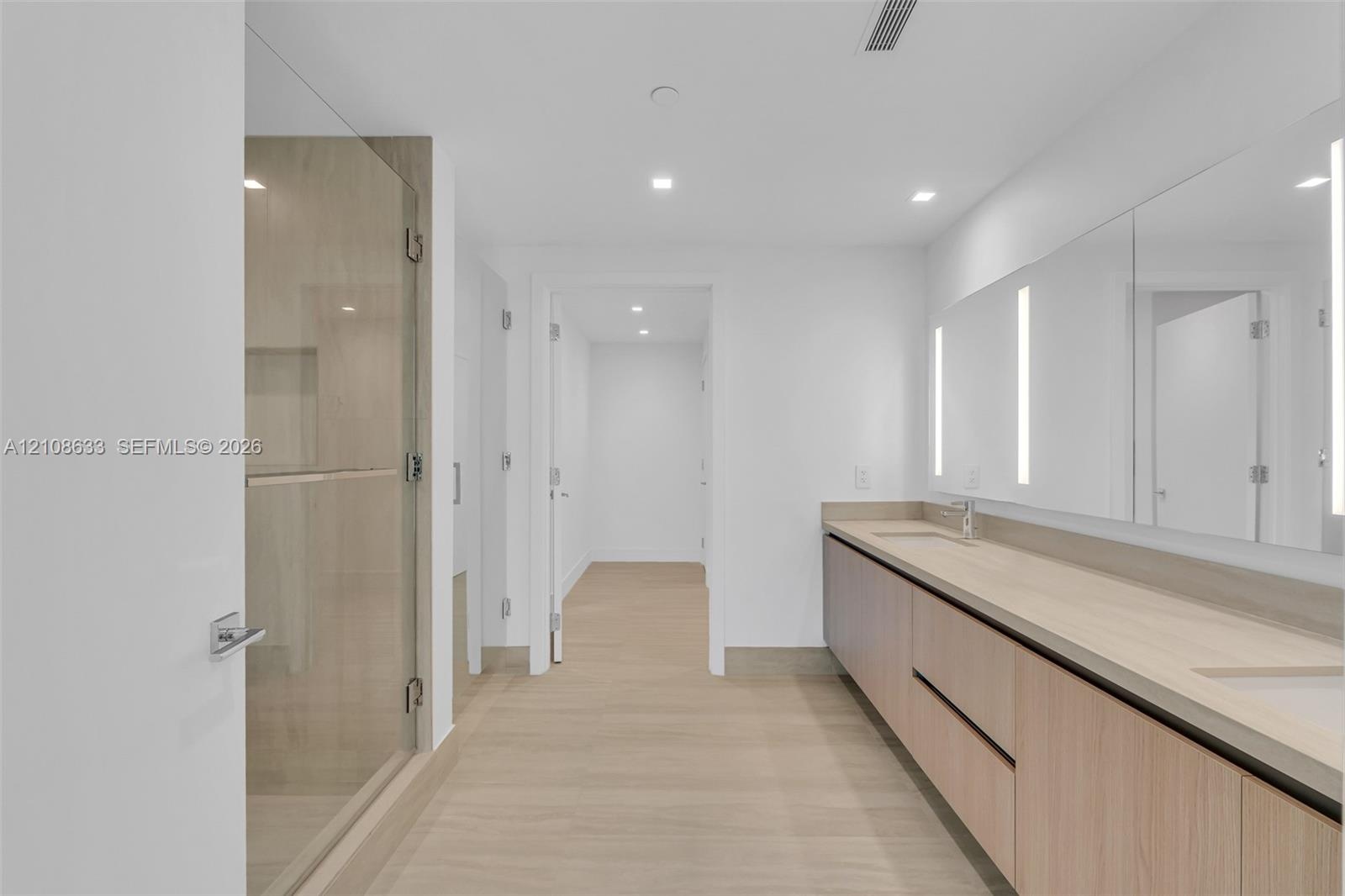 Floating wood-finish vanity with dual integrated sinks, light-toned countertop, floor-to-ceiling glass enclosed shower with integrated niche, and full
