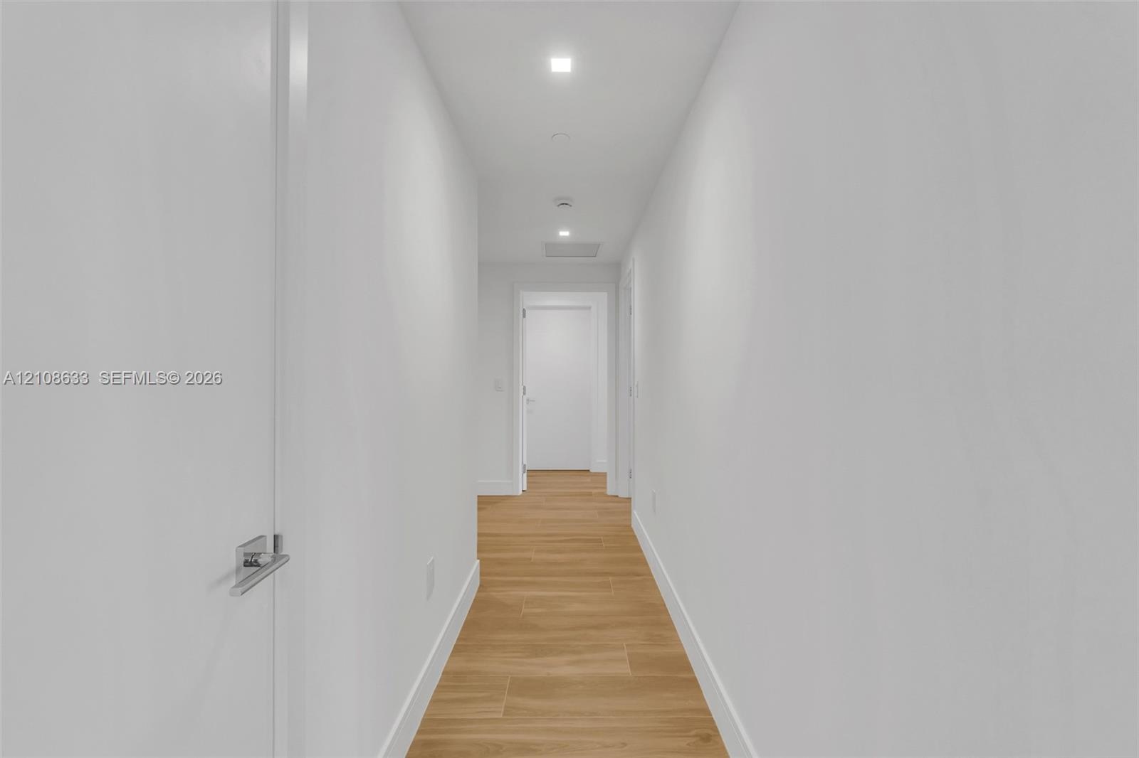 Hallway featuring wood-finish flooring, recessed lighting, and interior doors with brushed metal lever hardware