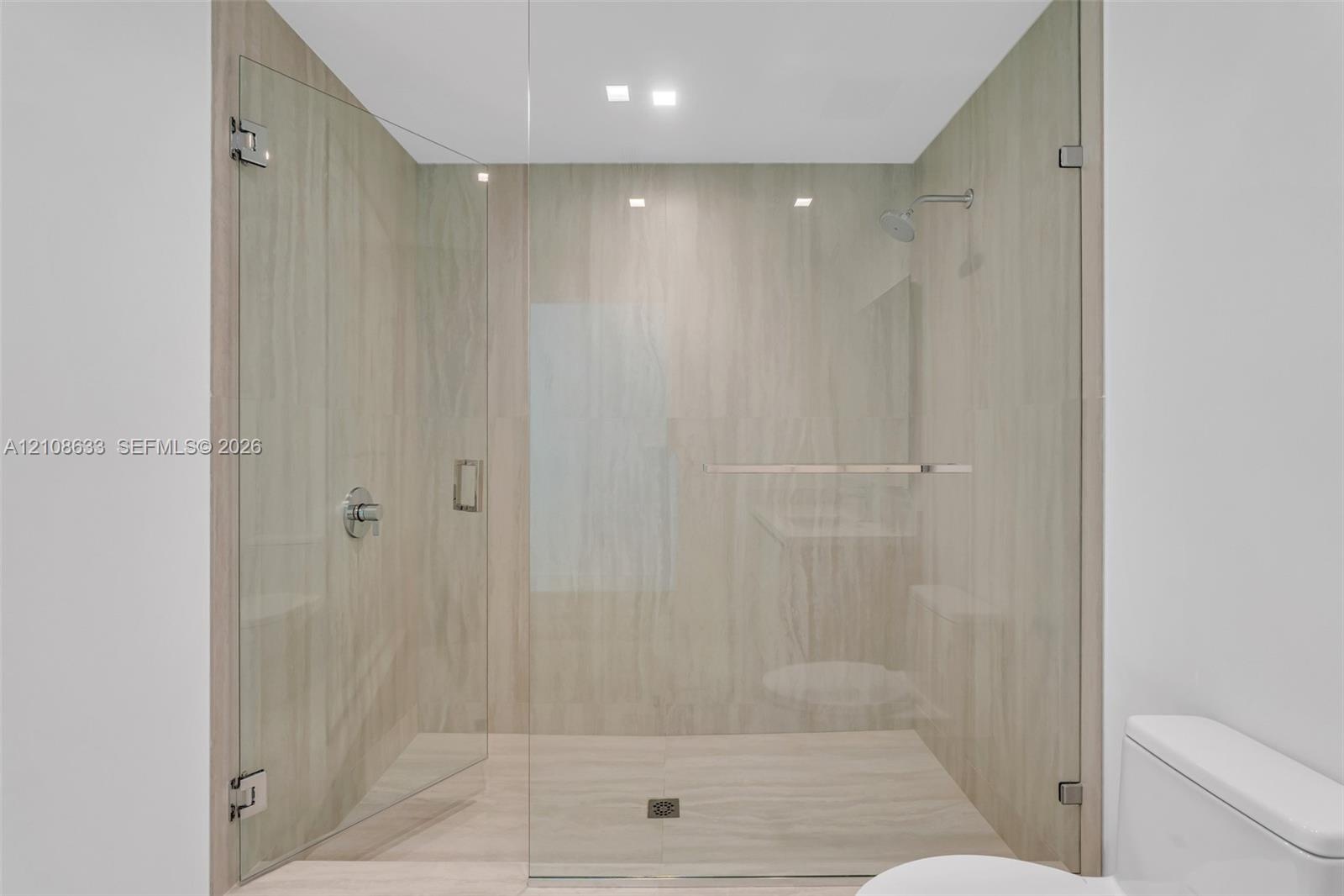 Walk-in shower featuring floor-to-ceiling large-format tile, frameless glass enclosure, recessed lighting, and chrome shower fixtures