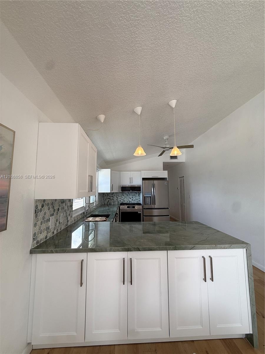 Kitchen featuring white shaker-style cabinetry, solid-surface countertops with waterfall edge, geometric tile backsplash, stainless steel appliances, 