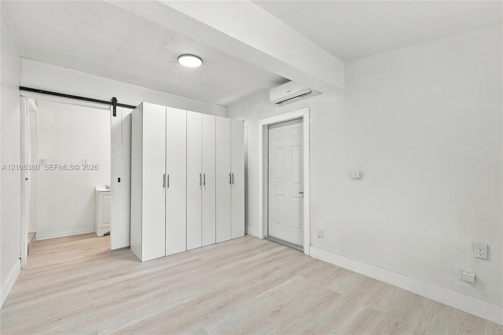 Interior space featuring light-toned wood-finish flooring, white built-in cabinetry, a sliding barn-style door, and a wall-mounted climate control uni