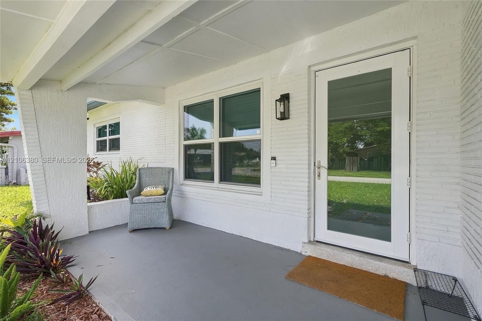 Covered front porch featuring painted brick exterior, concrete flooring, exterior wall-mounted lantern light fixture, and a full-light glass panel ent