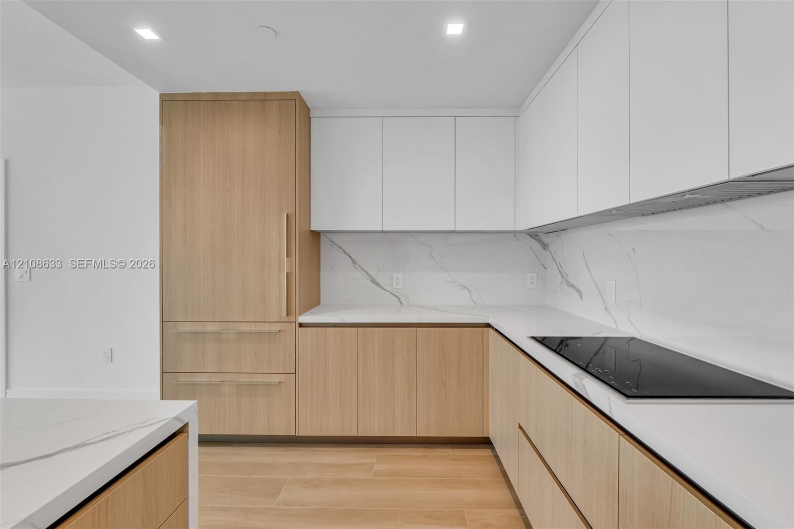 Modern kitchen featuring flat-panel wood-finish cabinetry, floor-to-ceiling refrigerator paneling, white solid-surface countertops, stone-patterned ba