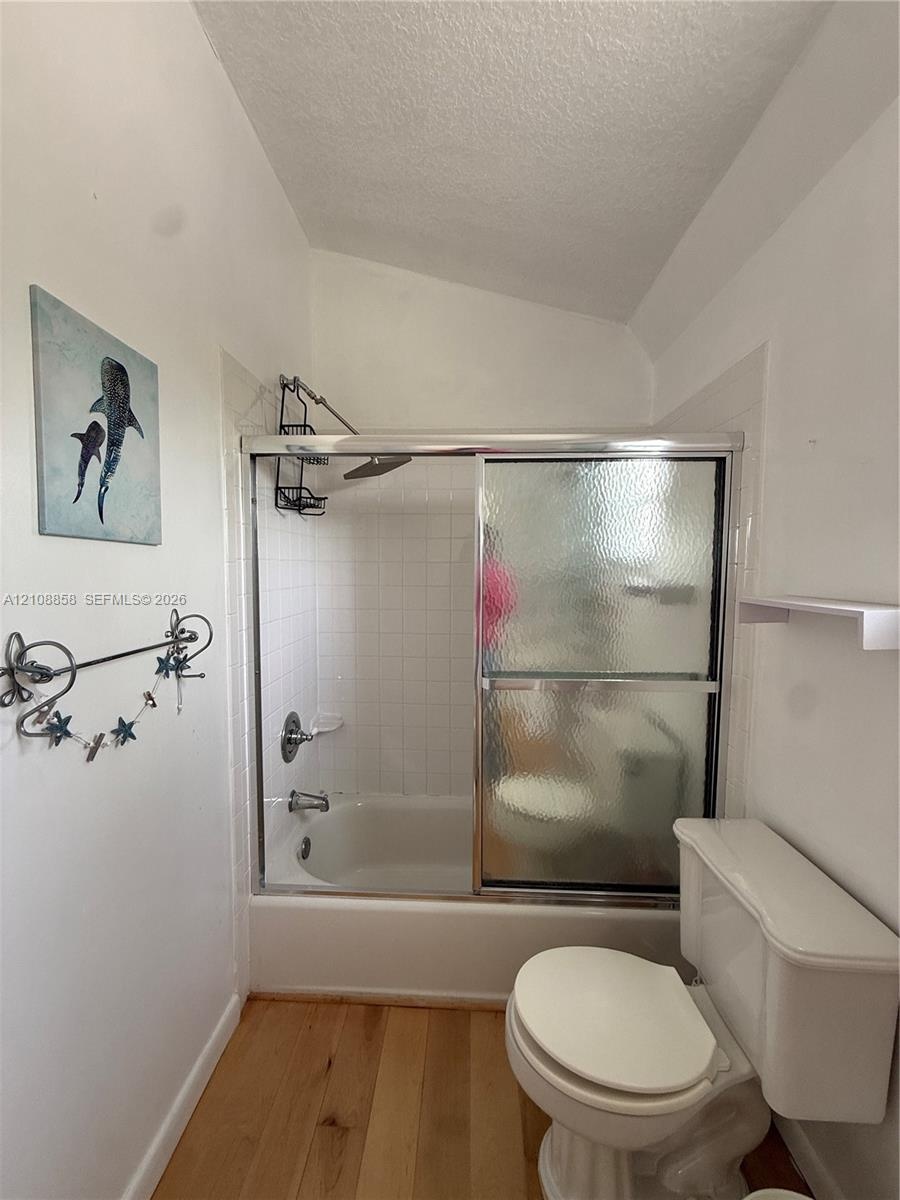 Bathroom featuring a shower-tub combination with white tile surround, glass sliding doors, and wood-finish flooring