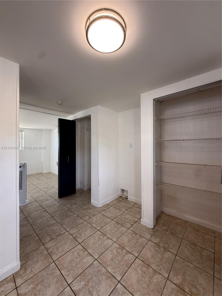 Neutral-toned ceramic tile flooring, built-in wire shelving, and a flush-mount circular ceiling fixture