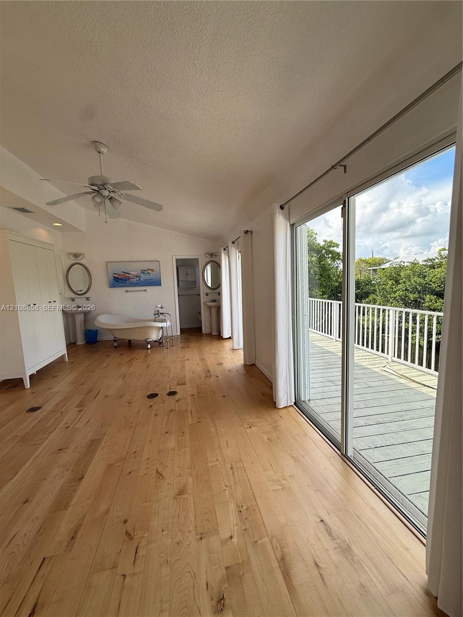 Wood-finish flooring, freestanding soaking tub, dual pedestal sinks with oval mirrors, and large sliding glass doors opening to a railed exterior deck
