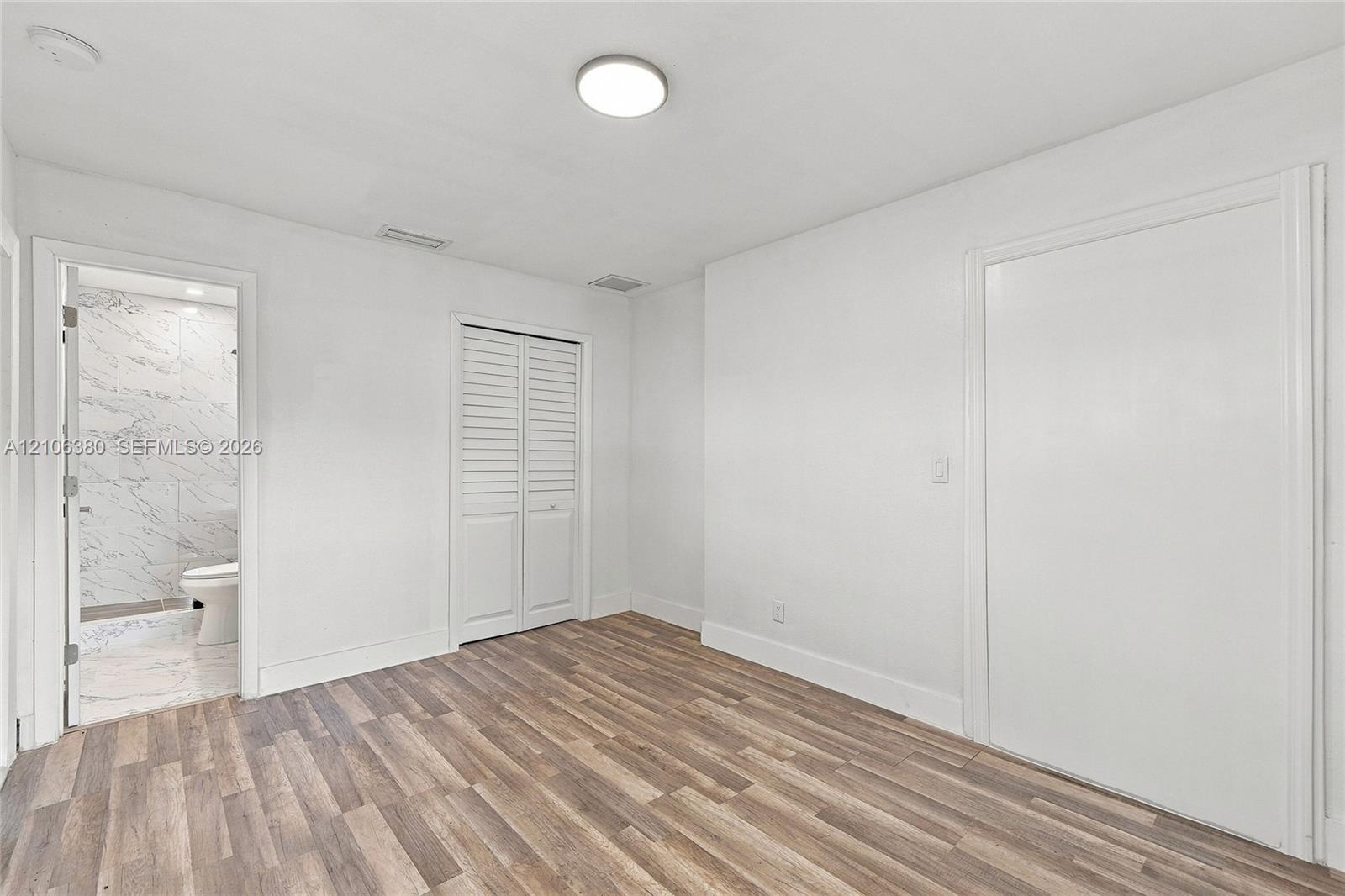 Room featuring wood-finish flooring, white louvered closet doors, a flat-panel door, and a surface-mount ceiling light fixture