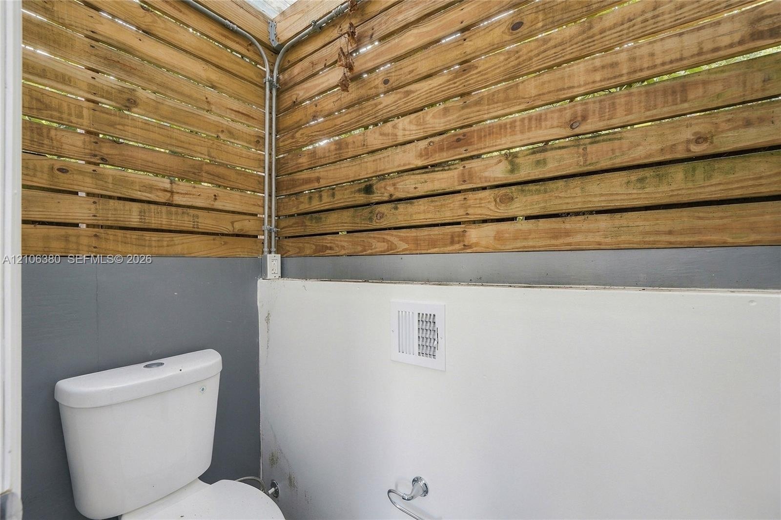 Privacy-fencing enclosure with horizontal wood slats, exposed conduit, and a white porcelain toilet