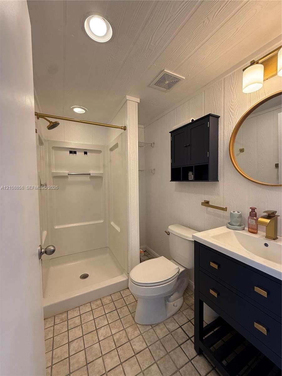Bathroom featuring a dark-toned vanity with integrated basin, brass-finish fixtures, oval wall mirror, built-in cabinet storage, and a walk-in shower 