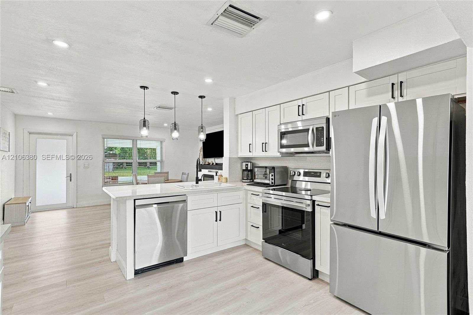 Kitchen featuring white shaker-style cabinetry, stainless steel appliances, quartz countertops, a peninsula with pendant lighting, and light-toned woo
