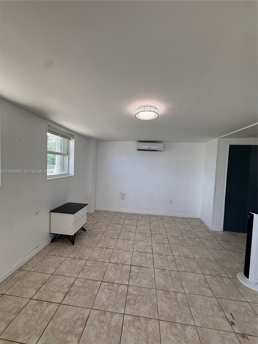 Interior space featuring neutral tile flooring, a wall-mounted mini-split HVAC system, a flush-mount circular light fixture, and a window with a horiz