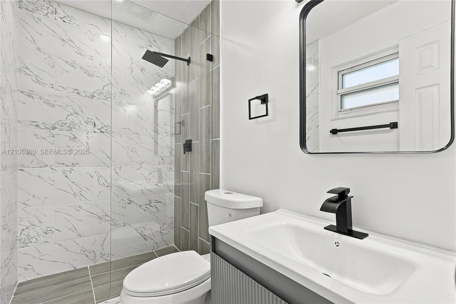 Bathroom featuring a glass-enclosed shower with marbled tile, a rain-style showerhead, wood-finish wall tile accents, a vanity with a rectangular basi