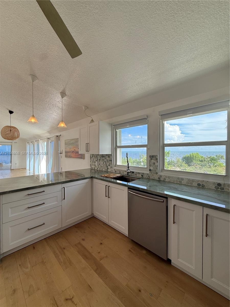 Kitchen featuring white shaker-style cabinetry, stone-finish countertops, stainless steel dishwasher, hexagonal tile backsplash, and wood-finish floor