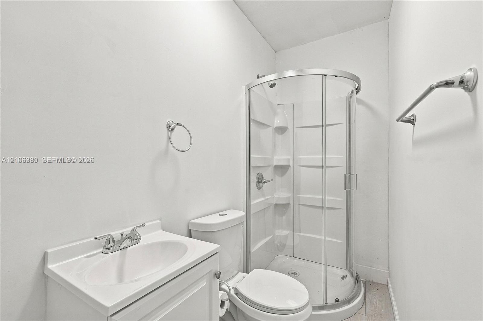 Bathroom featuring a corner shower enclosure with a molded surround, white pedestal vanity with dual-handle faucet, and chrome hardware throughout