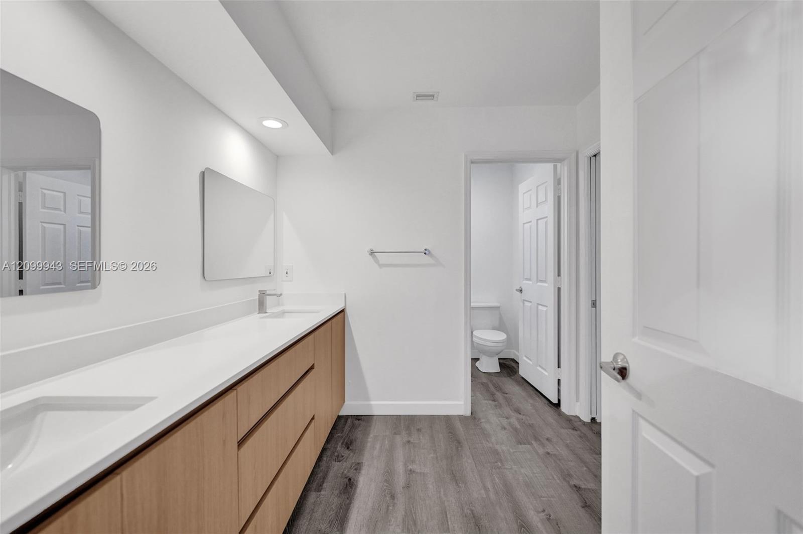 Bathroom featuring a long wood-finish vanity with a solid-surface countertop, dual undermount sinks, wall-mounted rectangular mirrors, and wood-finish