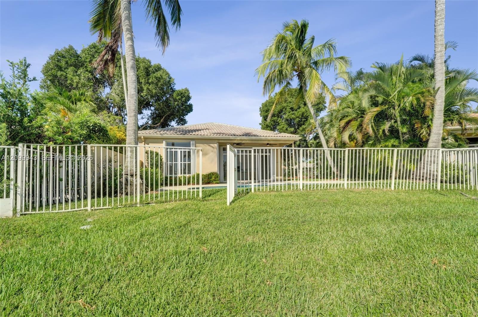 Rear exterior featuring a tile roof, stucco siding, a fenced-in yard, and mature palm trees