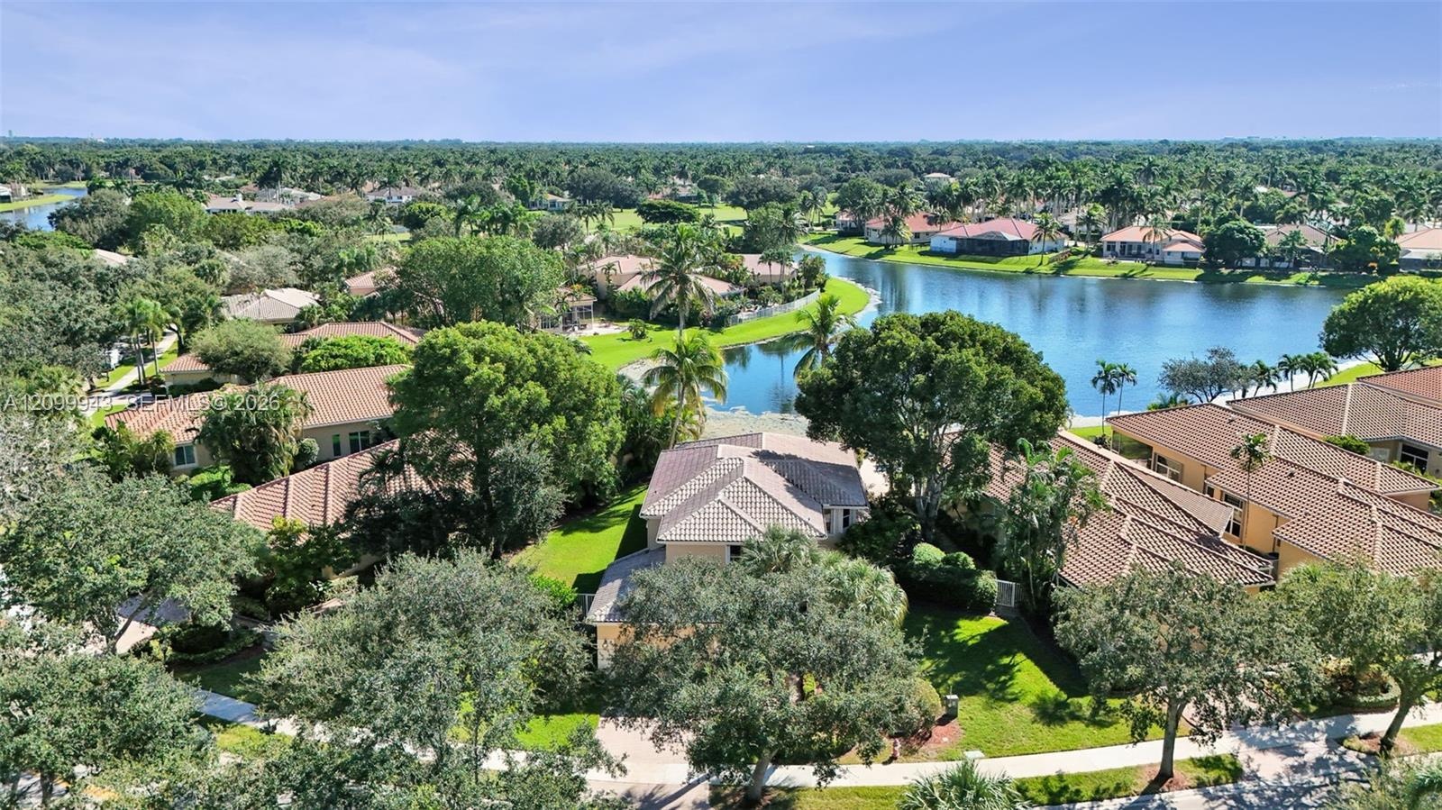 Aerial perspective of a residential neighborhood featuring tiled rooflines, mature landscaping, expansive green spaces, and an integrated freshwater l