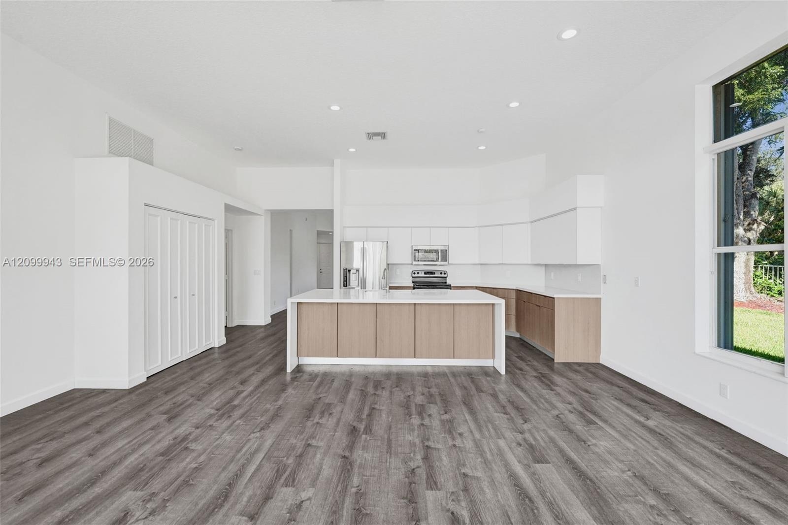 Kitchen featuring white flat-panel cabinetry, wood-finish lower cabinets, stone-surfaced kitchen island, wood-finish flooring, and recessed lighting