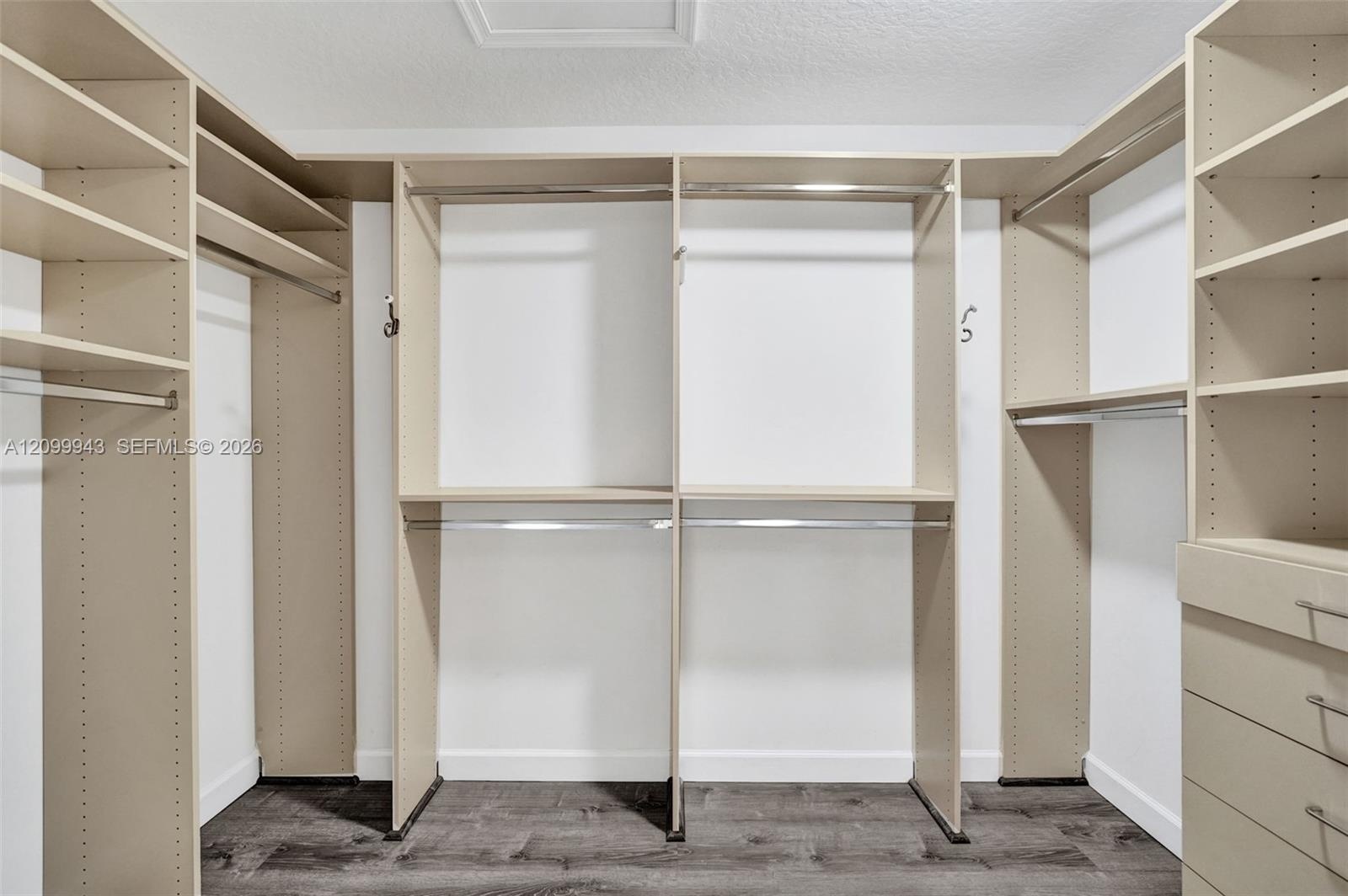 Custom walk-in closet featuring extensive built-in shelving, integrated hanging rods, and a multi-drawer storage unit with wood-finish flooring