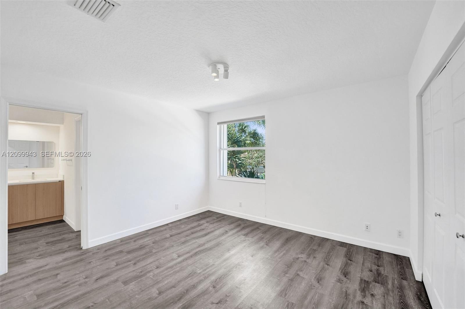 Neutral-toned interior space featuring wood-finish flooring, a double-door closet with paneled hardware, a single-light window, and modern multi-direc